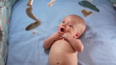 Çocuk, bebek beşiğinin üzerinde dönen el yapımı yumuşak oyuncaklarla müzikal bebek hareketine bakıyor..