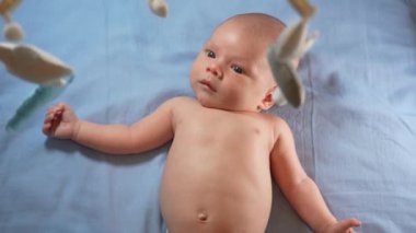 Çocuk, bebek beşiğinin üzerinde dönen el yapımı yumuşak oyuncaklarla müzikal bebek hareketine bakıyor..
