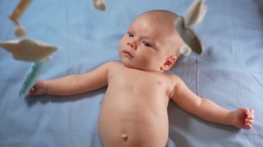 Çocuk, bebek beşiğinin üzerinde dönen el yapımı yumuşak oyuncaklarla müzikal bebek hareketine bakıyor..