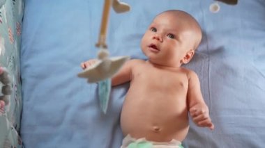 Çocuk, bebek beşiğinin üzerinde dönen el yapımı yumuşak oyuncaklarla müzikal bebek hareketine bakıyor..