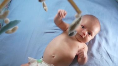 Çocuk, bebek beşiğinin üzerinde dönen el yapımı yumuşak oyuncaklarla müzikal bebek hareketine bakıyor..