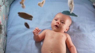 Çocuk, bebek beşiğinin üzerinde dönen el yapımı yumuşak oyuncaklarla müzikal bebek hareketine bakıyor..