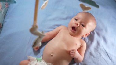 Çocuk, bebek beşiğinin üzerinde dönen el yapımı yumuşak oyuncaklarla müzikal bebek hareketine bakıyor..