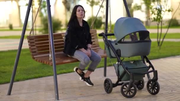 Maman avec une poussette est assise sur une balançoire dans la cour d'un immeuble résidentiel — Video