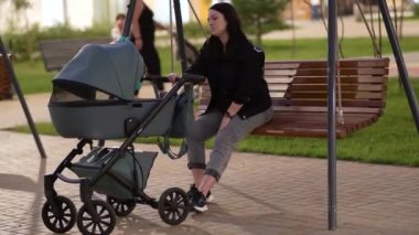 Elinde bebek arabası olan annem bir apartmanın avlusunda salıncakta oturuyor.