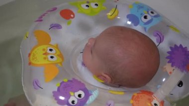 Bir çocuk şişme halkalı bir küvette banyo yapıyor. Küçük bir çocuk banyoda yüzüyor..