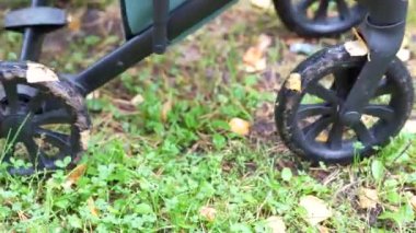 Sonbaharda yaprakların ve su birikintilerinin üzerinde giden bir bebek arabasının tekerlerinin yakın çekimi.