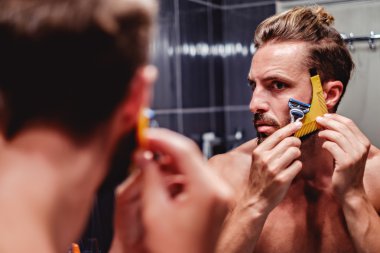 Man shaving his beard in the bathroom clipart