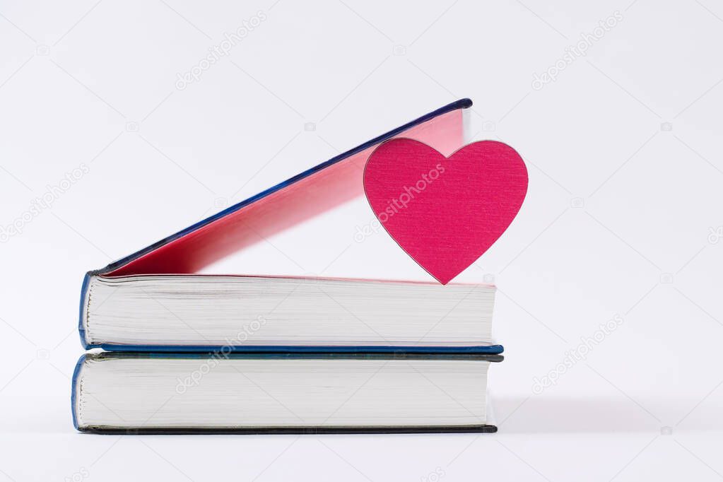 Two books lie on a white background. A pink heart stands between the pages in the top book. Book reading concept.