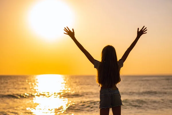 長い髪の少女が手を上げて海岸に立っている 女の子は美しい夕日を見て — ストック写真