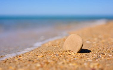 Deniz kıyısında düz küçük bir taş duruyor. Taşın üzerine yazı için yer. Arka planda deniz. Deniz eğlencesi teması üzerine bir yazı için boşluk.