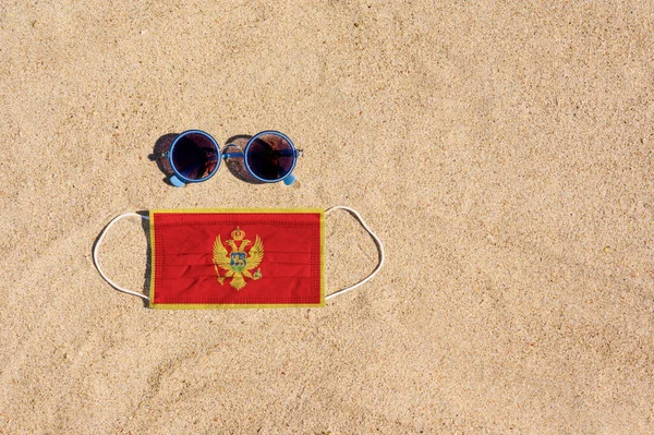 Lékařská Maska Barvě Černohorské Vlajky Leží Písečné Pláži Vedle Sklenic — Stock fotografie