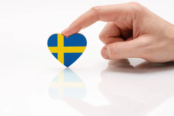 スウェーデンへの愛と尊敬 男性の手は白いガラスの表面にスウェーデンの旗の形に心を持っています スウェーデンの愛国心と誇りの概念 — ストック写真