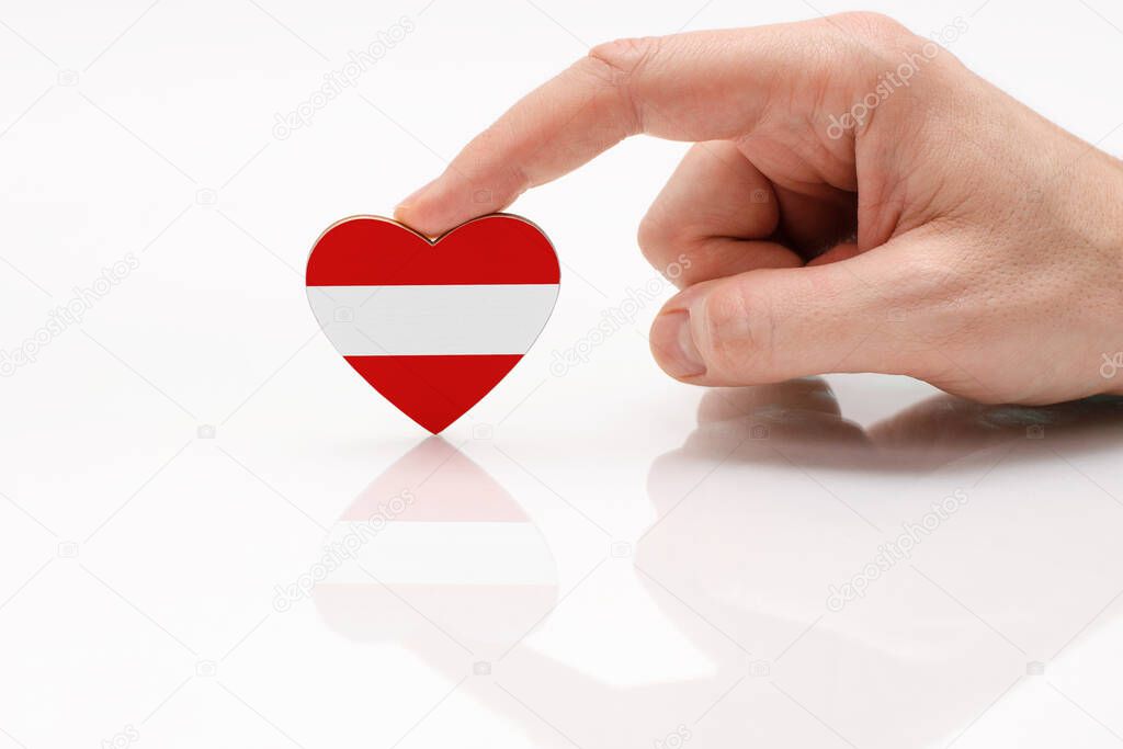 Love and respect Austria. A man's hand holds a heart in the shape of the Austria flag on a white glass surface. The concept of Austrian patriotism and pride.