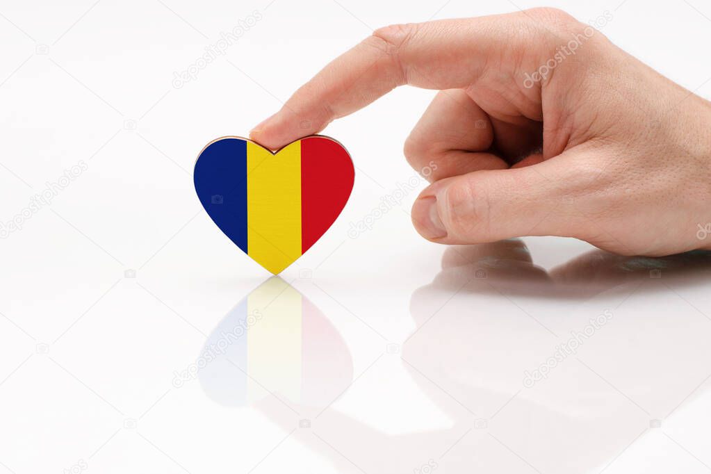 Love and respect Romania. A man's hand holds a heart in the shape of the Romania flag on a white glass surface. The concept of Romanian patriotism and pride.