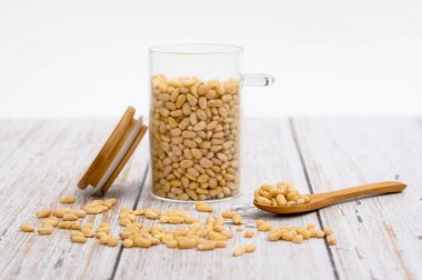 Masanın üzerinde çam fıstığı olan tahta kaşık. Yakınlarda fındık taneleri ve fındıklı cam bardak var. Bir kaşık dolusu fındığa odaklan..