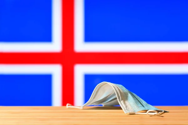 アイスランドの国旗を背景に 医療用マスクがテーブルの上に置かれています パンデミックの際のアイスランドの住民や観光客のための強制マスク制度の概念 — ストック写真