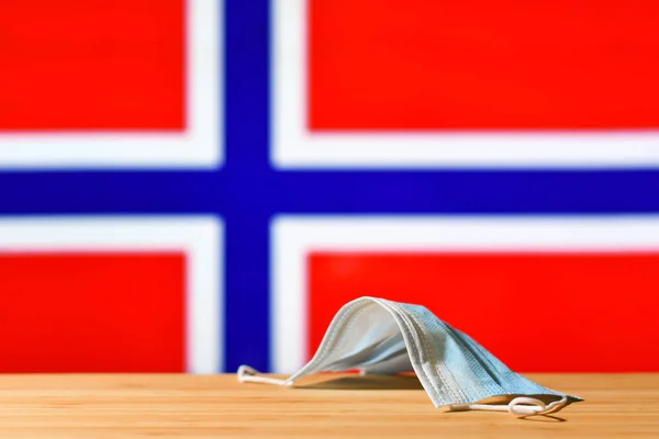 ノルウェーの国旗を背景に医療用マスクがテーブルの上に置かれている パンデミック時のノルウェーの住民と観光客のための強制マスク制度の概念 — ストック写真