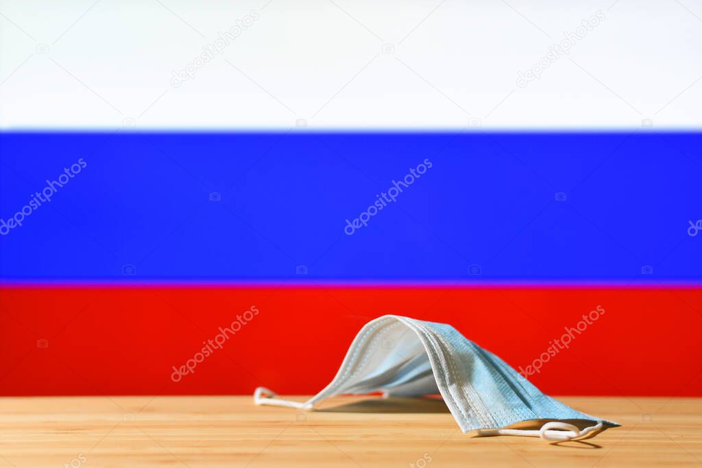 A medical mask lies on the table against the background of the flag of Russia. The concept of a mandatory mask regime for residents of the country and tourists in Russia during a pandemic.
