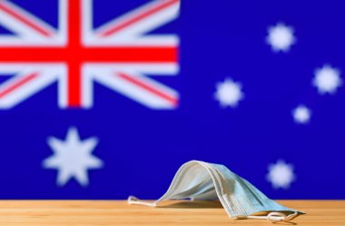 Avustralya bayrağının arka planında bir tıbbi maske yatmaktadır. Bir salgın sırasında ülke sakinleri ve Avustralya 'daki turistler için zorunlu maske rejimi kavramı.