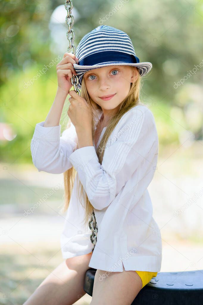 Close-up portrait of a beautiful girl sitting on a swing in summer. Vertical kids in summer