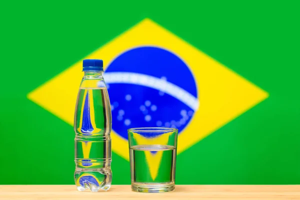Бутылка Чистой Питьевой Воды Стакан Стоят Столе Фоне Флага Бразилии — стоковое фото