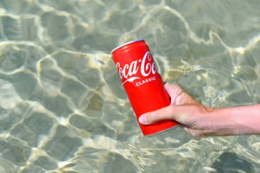 Anapa, Russia - July 2021: A can of Coca-Cola drink in hand is cooled in sea water