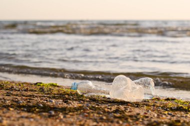 Gün batımında deniz kıyısında plastik çöpler. Deniz evi çöp kirliliği konsepti. Şişeye odaklan..
