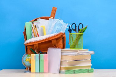 Çocukları okula hazırlıyorum. Okul ögeleri ve ders kitapları mavi arka planda tam okul çantasının yanında..