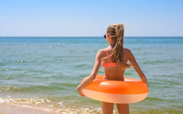 Dziewczyna Długimi Włosami Stoi Plaży Pomarańczowym Gumowym Pierścionkiem Patrzy Morze — Zdjęcie stockowe