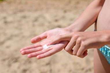 Beyaz güneş kremi bir çocuğun elinde kumlu bir plajın arka planında. Tatildeki çocuklar için güneş koruması