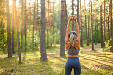 İnce, atletik bir kız kollarını kaldırıyor ve çam ormanında bir fitness kursuna hazırlanıyor. Seçici Odaklanma.