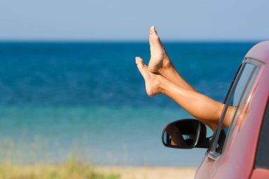Deniz ve kumsalın arka planındaki makine penceresinden güzel kadın bacakları. Otomobil yolculuğunun zevki.