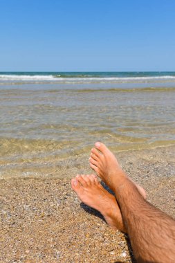 Sahilde, denizin yanında erkek ayakları. Dikey çekim ve bacaklara odaklanma.