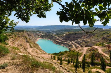 Dağlardaki güzel mavi göl. Güzel dağ manzarası. Kırım 'da madencilik malzemeleri için taş ocağı. Önde bir ağacın yeşil dalları var..