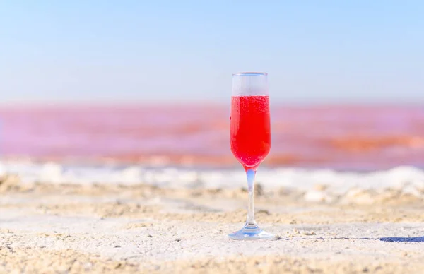 A glass with a pink drink on the white shore of a pink lake. Fabulous and romantic atmosphere. Selective focus on the glass.