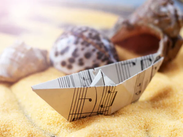 Model of a ship made of paper musical notes on the sand, seashell background