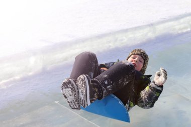 Küçük çocuk kışın buz slayt üzerinde binme keyfini çıkarın. Aile ile çocuklar için açık kış aktiviteleri.