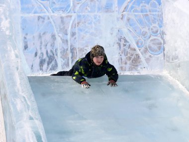 Küçük çocuk kışın buz slayt üzerinde binme keyfini çıkarın. Aile ile çocuklar için açık kış aktiviteleri.