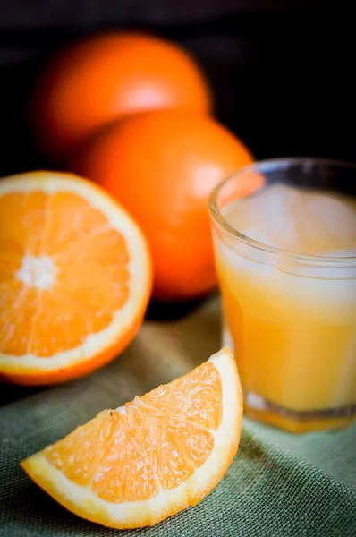 Glass of orange juice with ice and sliced oranges on wooden back — Stock Photo, Image