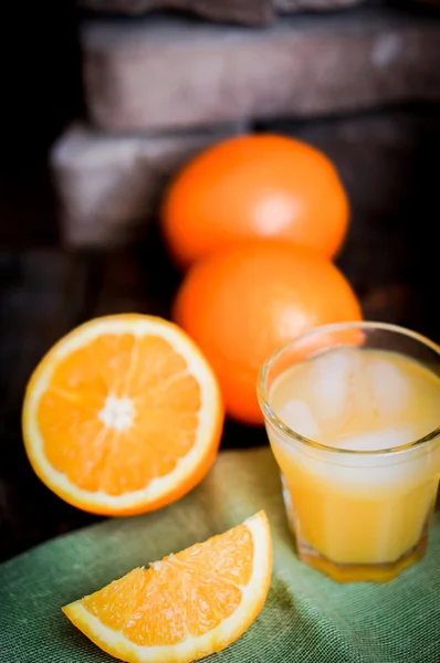 Glass of orange juice with ice and sliced oranges on wooden back — Stock Photo, Image