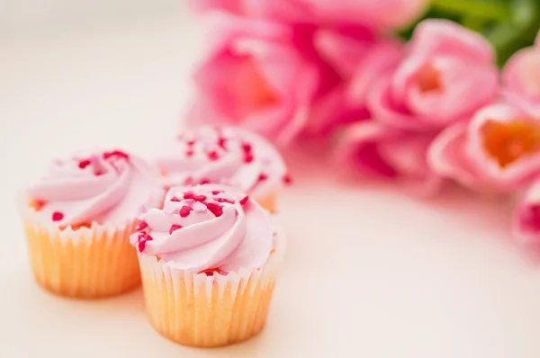 Cupcakes with pink cream,heart sprinkles and tulips on white tab — Stock Photo, Image