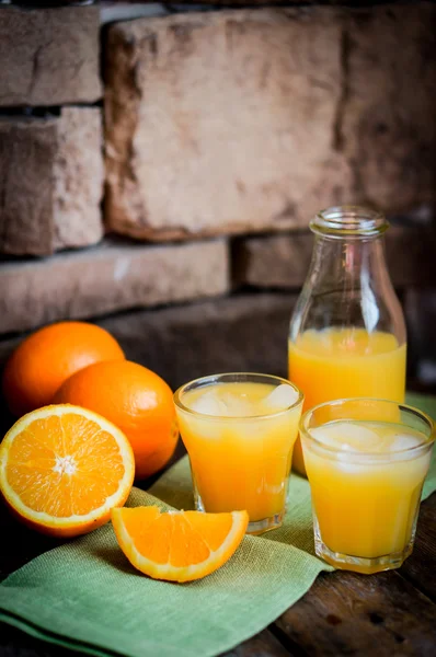 Glass of orange juice with ice and sliced oranges on wooden back — Stock Photo, Image