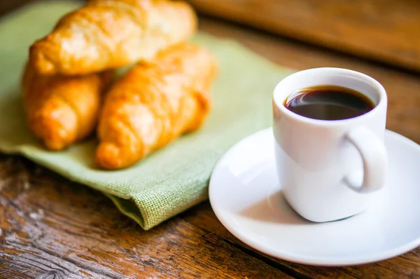 Schwarze Croissants mit schwarzem Kaffee auf hölzernem Hintergrund — Stockfoto