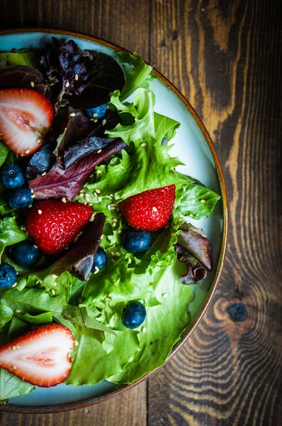 Ensalada verde con bayas sobre fondo de madera — Foto de Stock