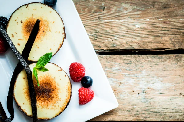 Brulee crema con varillas de vainilla y bayas sobre fondo de madera — Foto de Stock