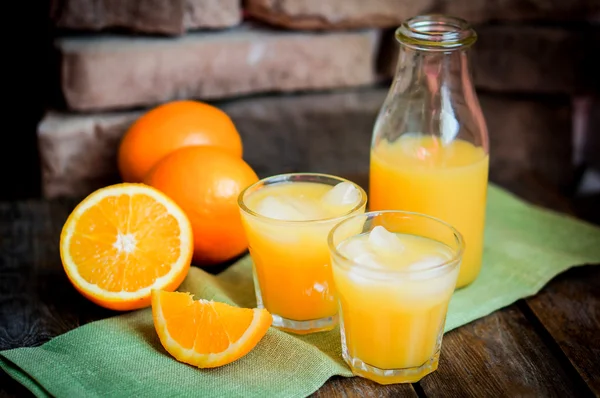Стакан апельсинового сока со льдом и нарезанные апельсины на деревянной спине — стоковое фото