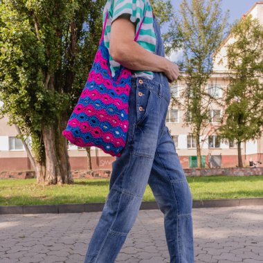 Şehir yürüyüşü sırasında şık, parlak örgü çantalı bir kadın. Çanta çiçek desenli mavi ve pembe örülmüş..