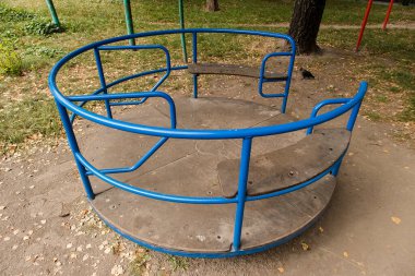 Güneşli bir parkta küçük mavi bir atlıkarınca, neşeli bir yaz atmosferi yaratıyor ve küçük çocuklar için açık hava eğlencesi sunuyor..