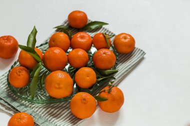 Beyaz arka plandaki cam tepside parlak mandalinalar doğal meyveyi, sadeliği ve sağlıklı yaşamı temsil ediyor. Boşluğu kopyala.